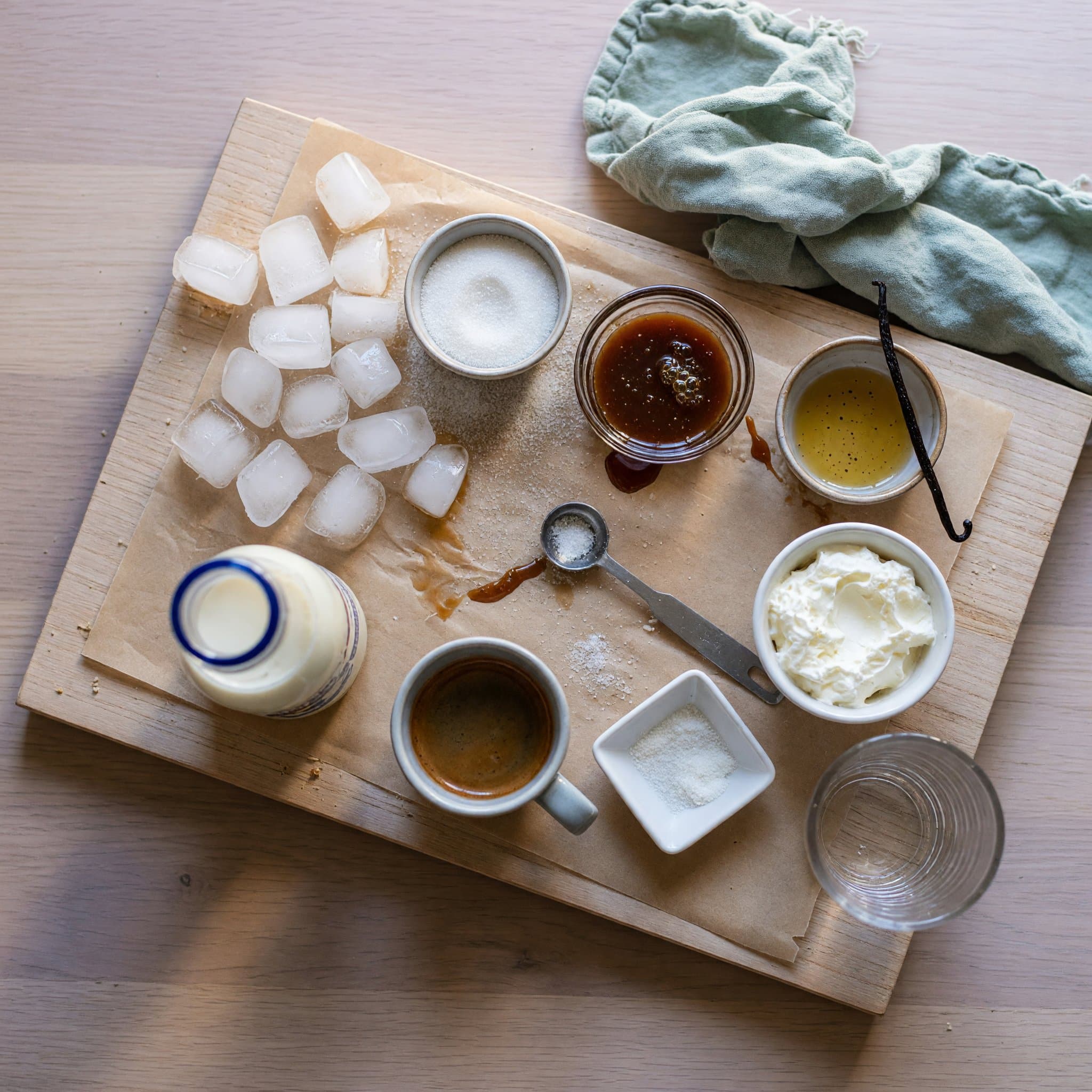 Overhead view of Ice, Milk, Caramel Sauce, Granulated Sugar, Vanilla Bean Extract, Xanthan Gum, Whipped Cream and Caramel Sauce arranged on a table