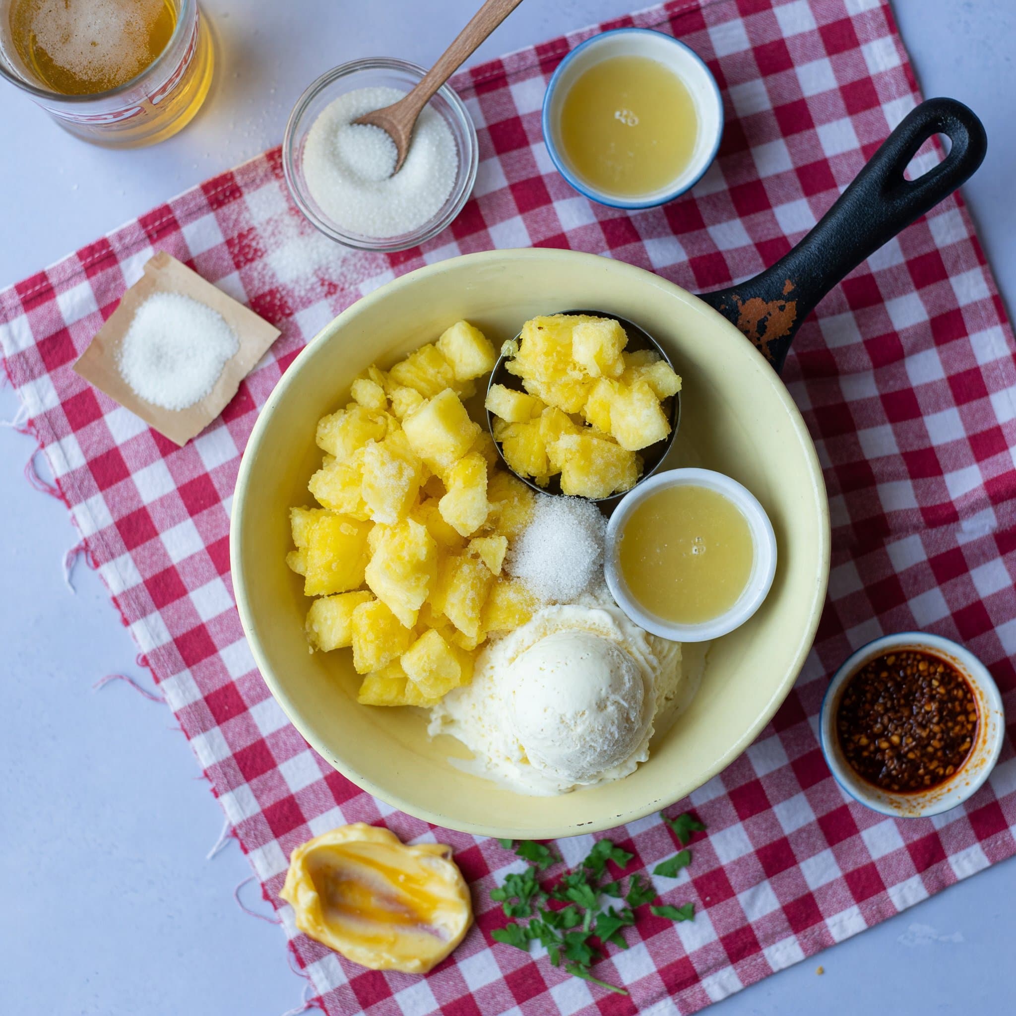 Overhead view of Granulated Sugar, Pineapple Juice, ice cream (vanilla) and frozen pineapple (heaping cups) arranged on a table