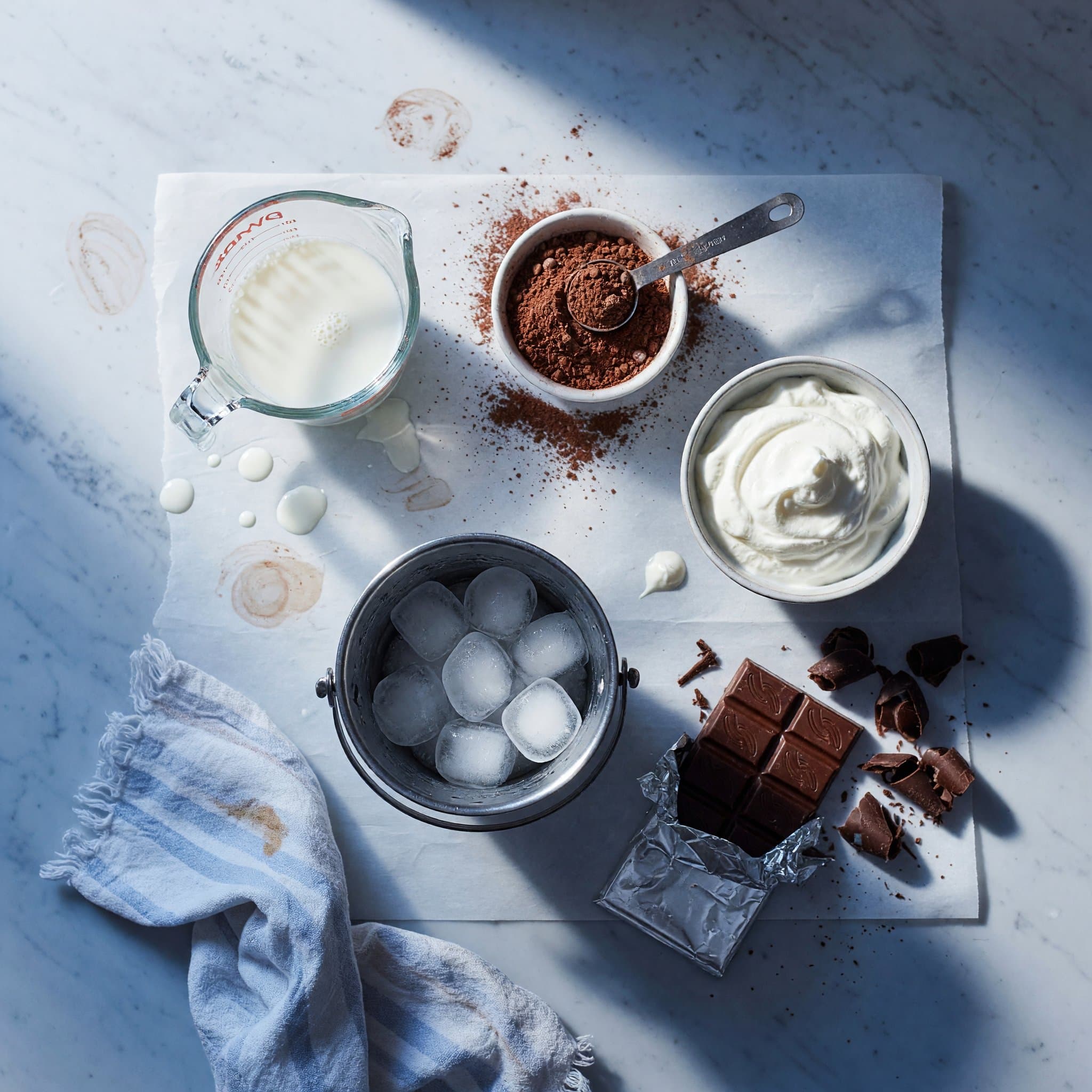 Overhead view of Milk, Hot Cocoa Mix, Ice, Whipped Cream and Chocolate Curls arranged on a table
