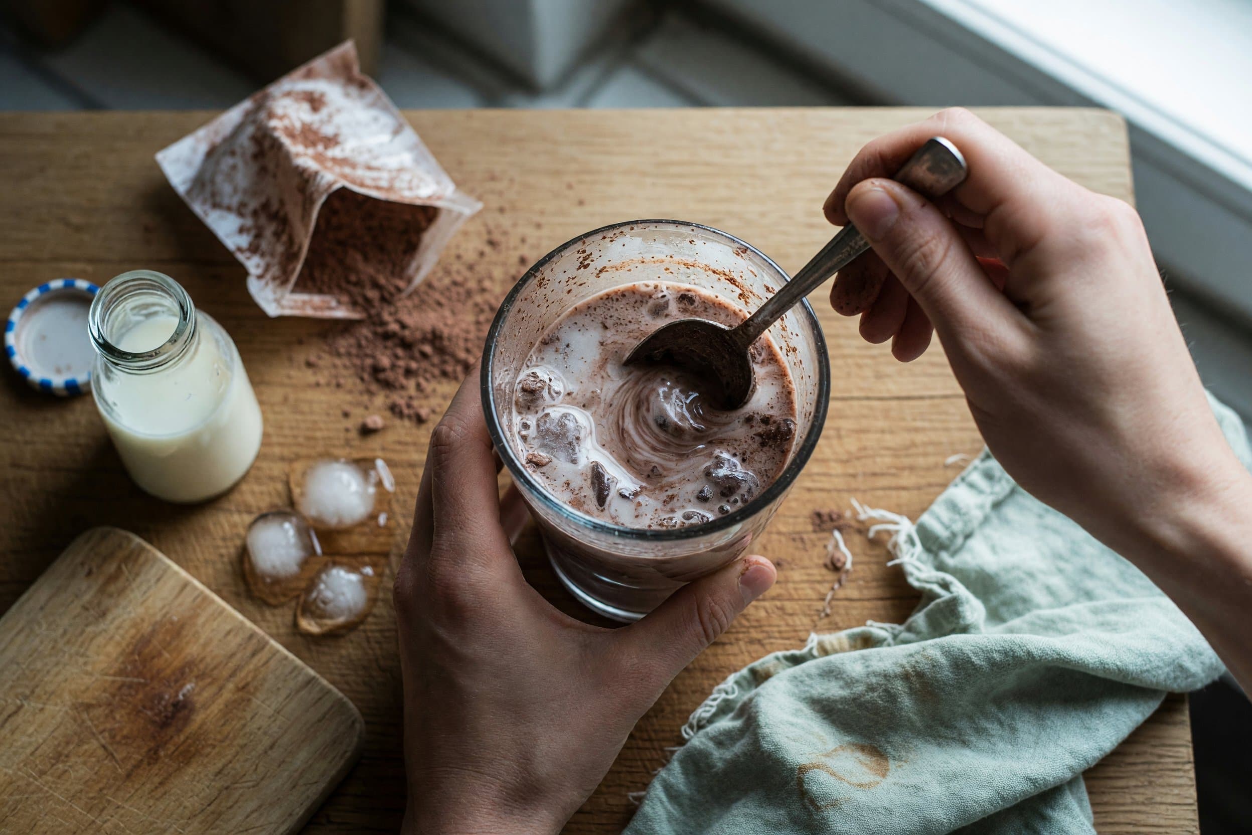 Stirring milk, hot cocoa mix, and ice while preparing Frozen Hot Chocolate Recipe