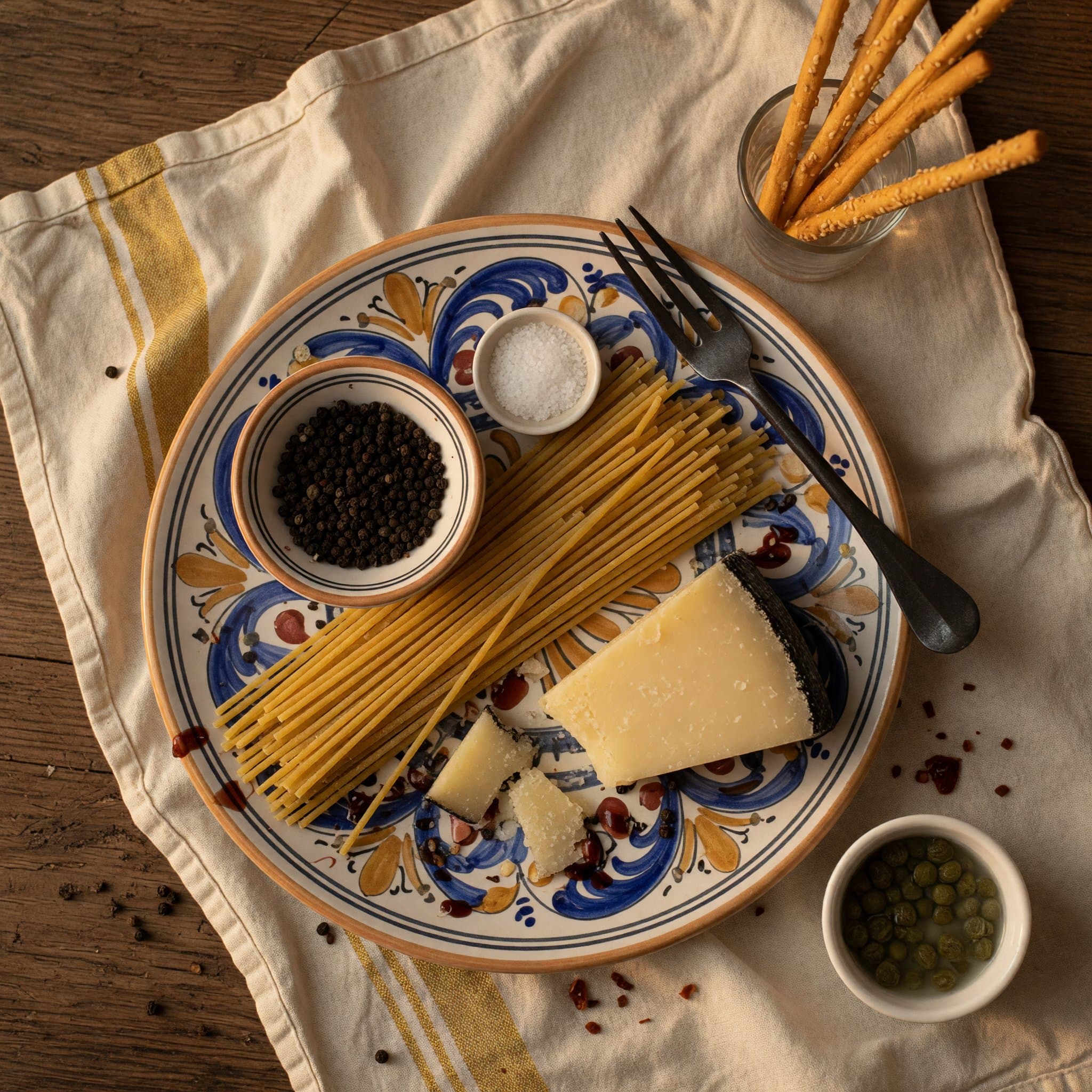 Overhead view of Spaghetti, Black Peppercorns, Salt and Pecorino Romano arranged on a table