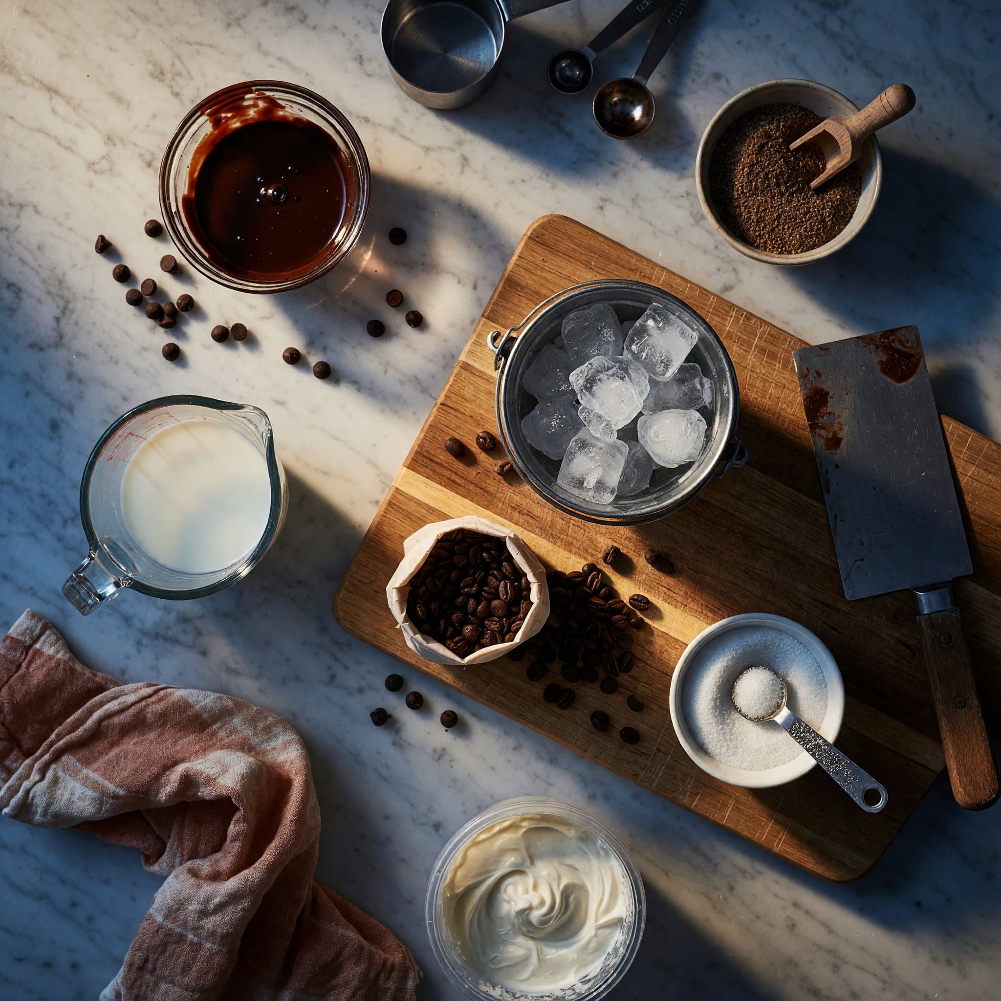 Overhead view of Coffee, Milk, Sugar, Chocolate Syrup, Mini Chocolate Chips, Ice and Whipped Topping arranged on a table