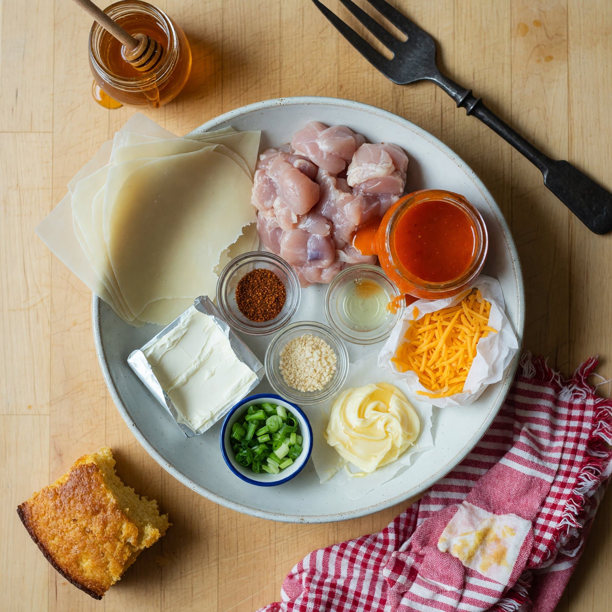 Overhead view of Egg Roll Wrappers, Chicken, Cream Cheese (Softened ), Cheddar Cheese (Shredded) and Buffalo Sauce arranged on a table