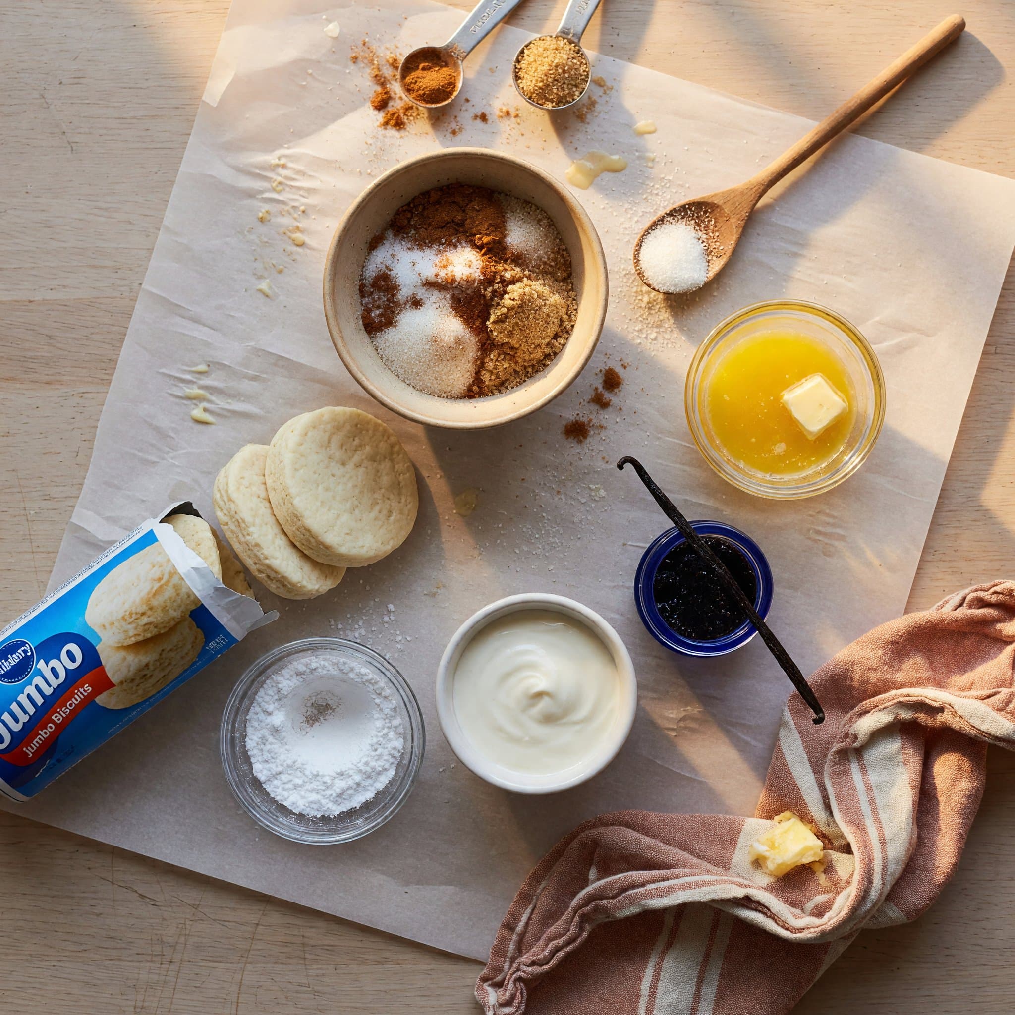 Overhead view of Granulated Sugar, Light Brown Sugar, Cinnamon, Unsalted Butter, (16 Ounce) Refrigerated Jumbo Biscuits, Powdered Sugar, Heavy Cream and Vanilla Bean Paste ((Or Vanilla Extract)) arranged on a table