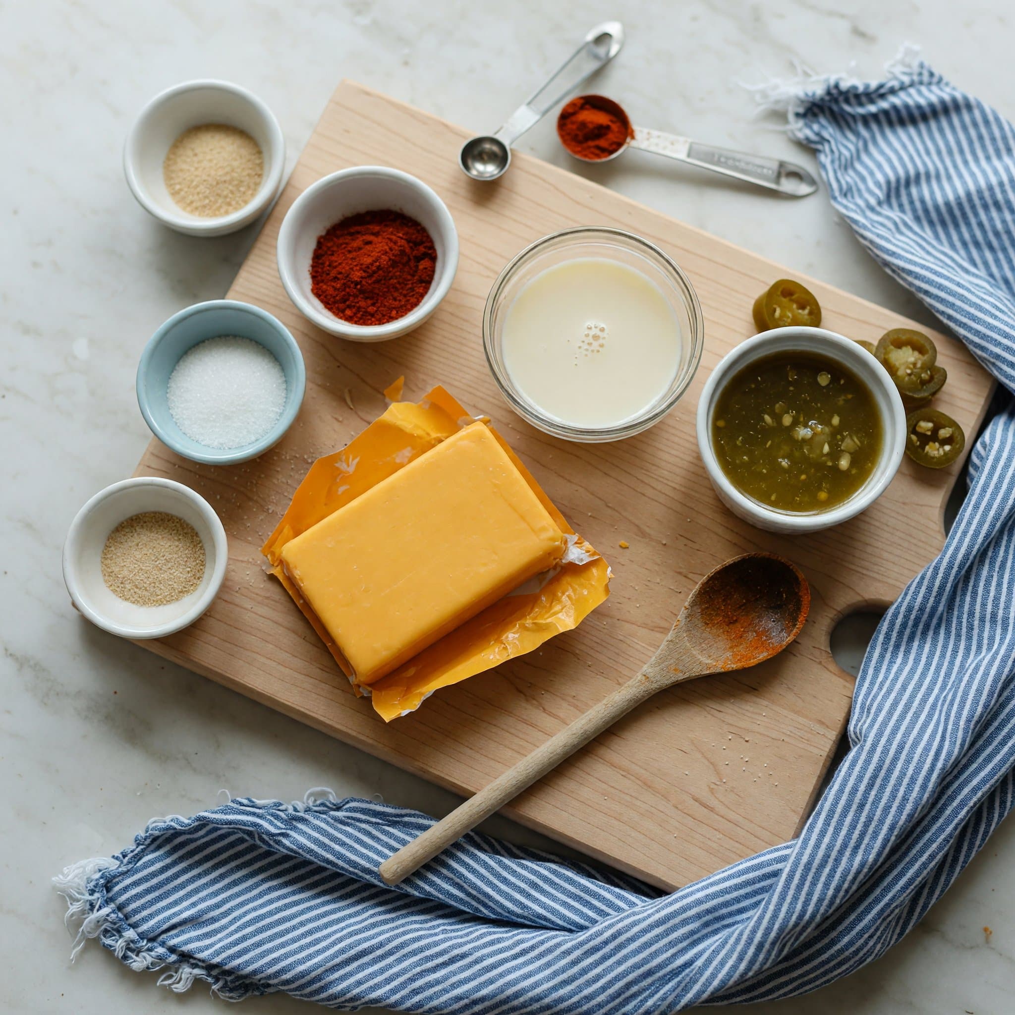 Overhead view of Velveeta Cheese, Evaporated Milk, Pickled Jalapeno Brine, Cayenne Pepper, Granulated Sugar and Garlic Powder arranged on a table