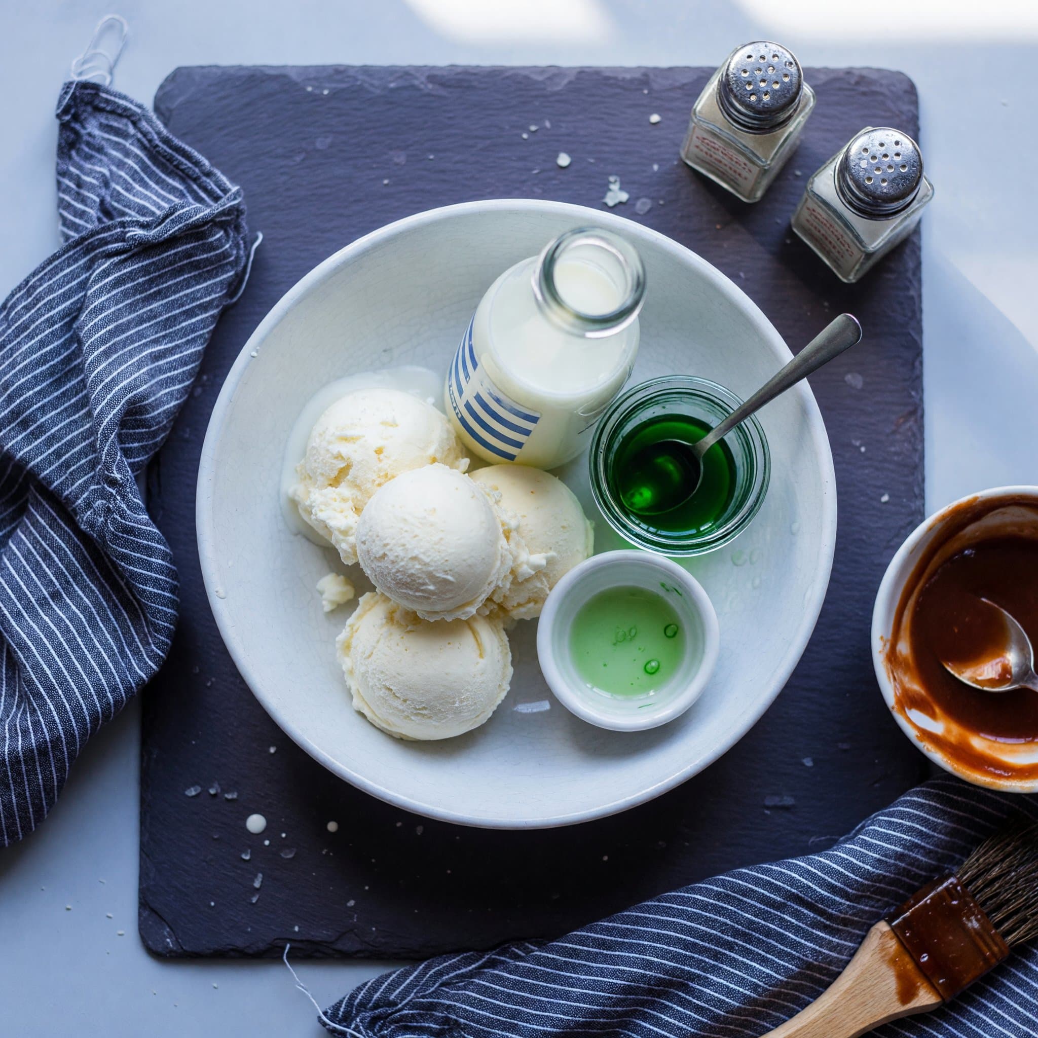 Overhead view of ice cream (vanilla ), Milk, Mint Extract and Green Food Coloring arranged on a table