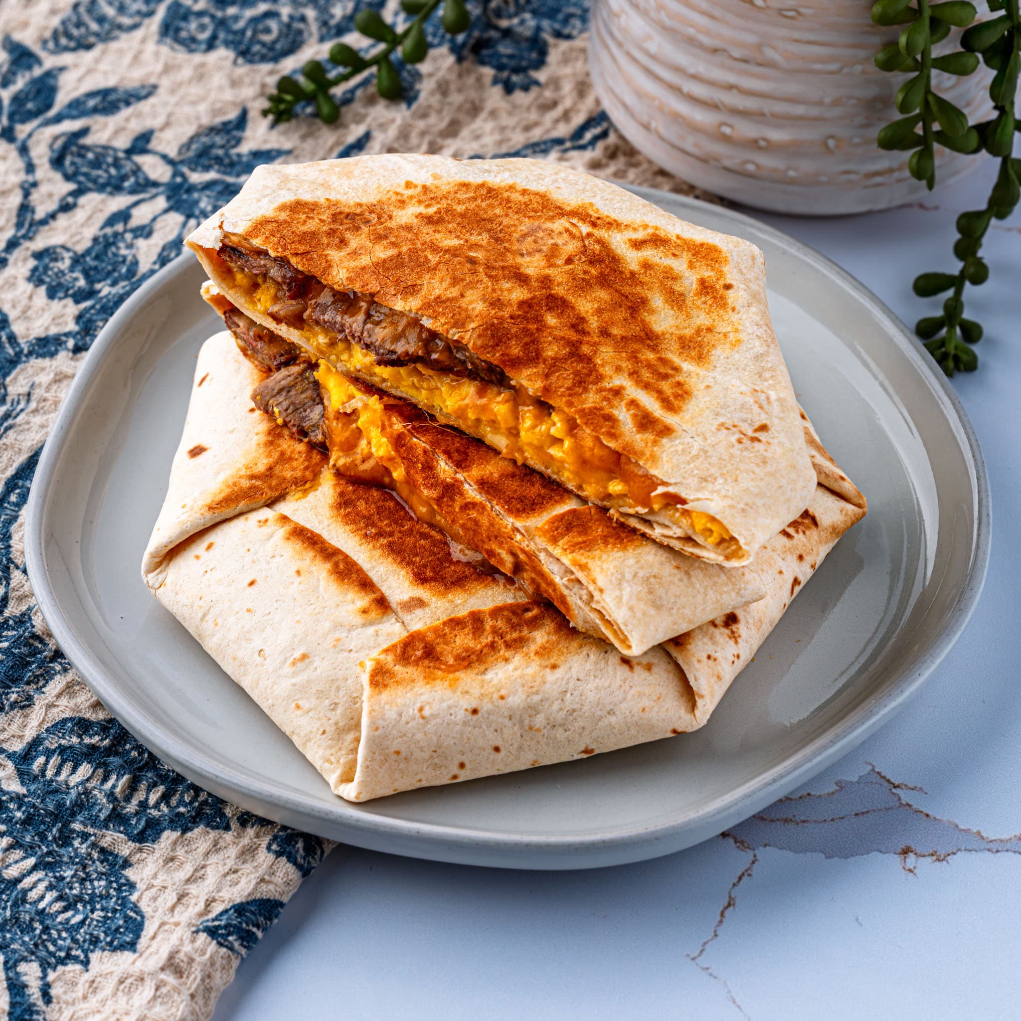 A golden, pan-seared crunchwrap sliced open to show the steak, egg, and cheese layers inside.