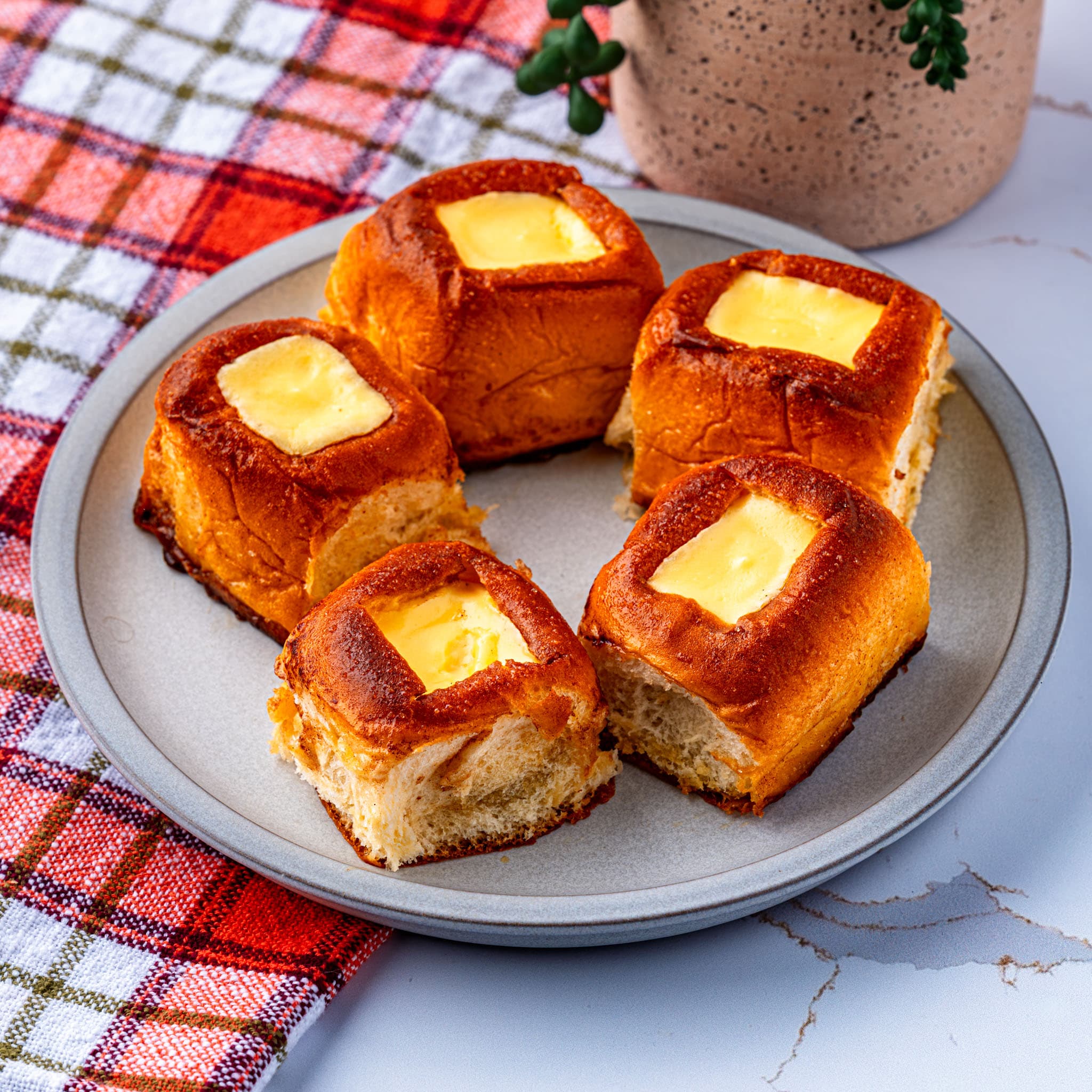 Golden Hawaiian rolls topped with creamy cheesecake filling and powdered sugar glaze, ready to eat.