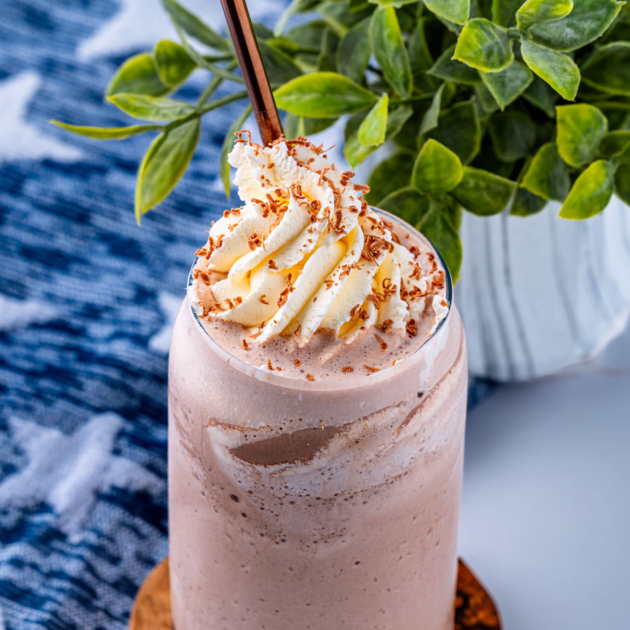 A tall glass of frozen hot chocolate topped with whipped cream and chocolate curls.