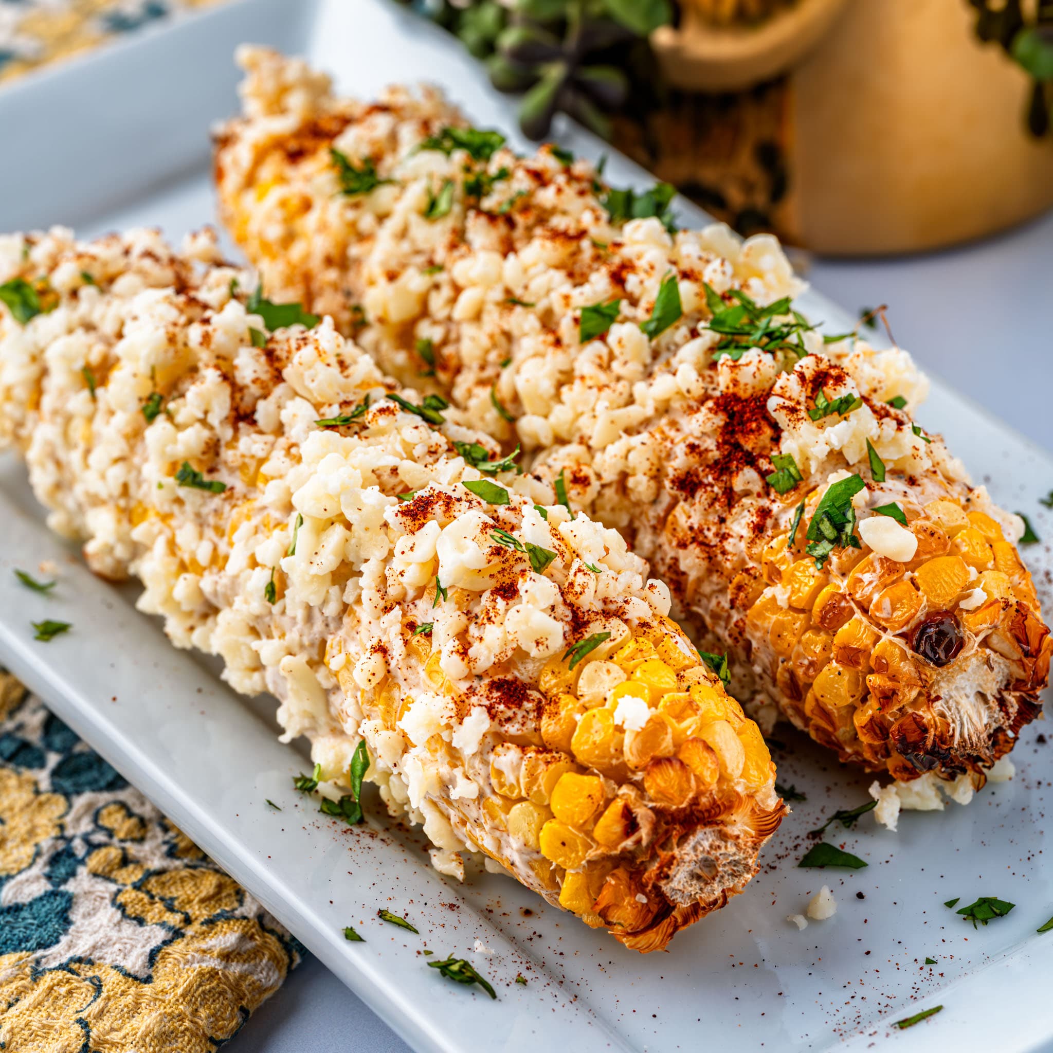 Four ears of air-fried corn coated in creamy sour cream sauce, crumbly cotija cheese, and fresh cilantro.