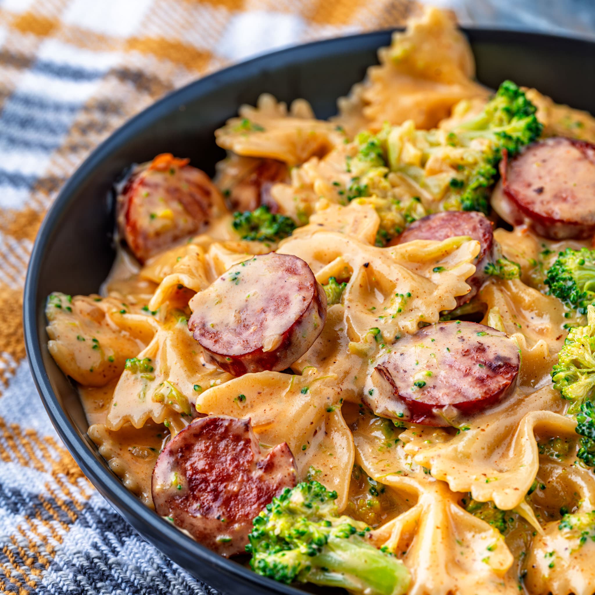 A skillet of bow tie pasta coated in cheddar sauce with sausage and broccoli.