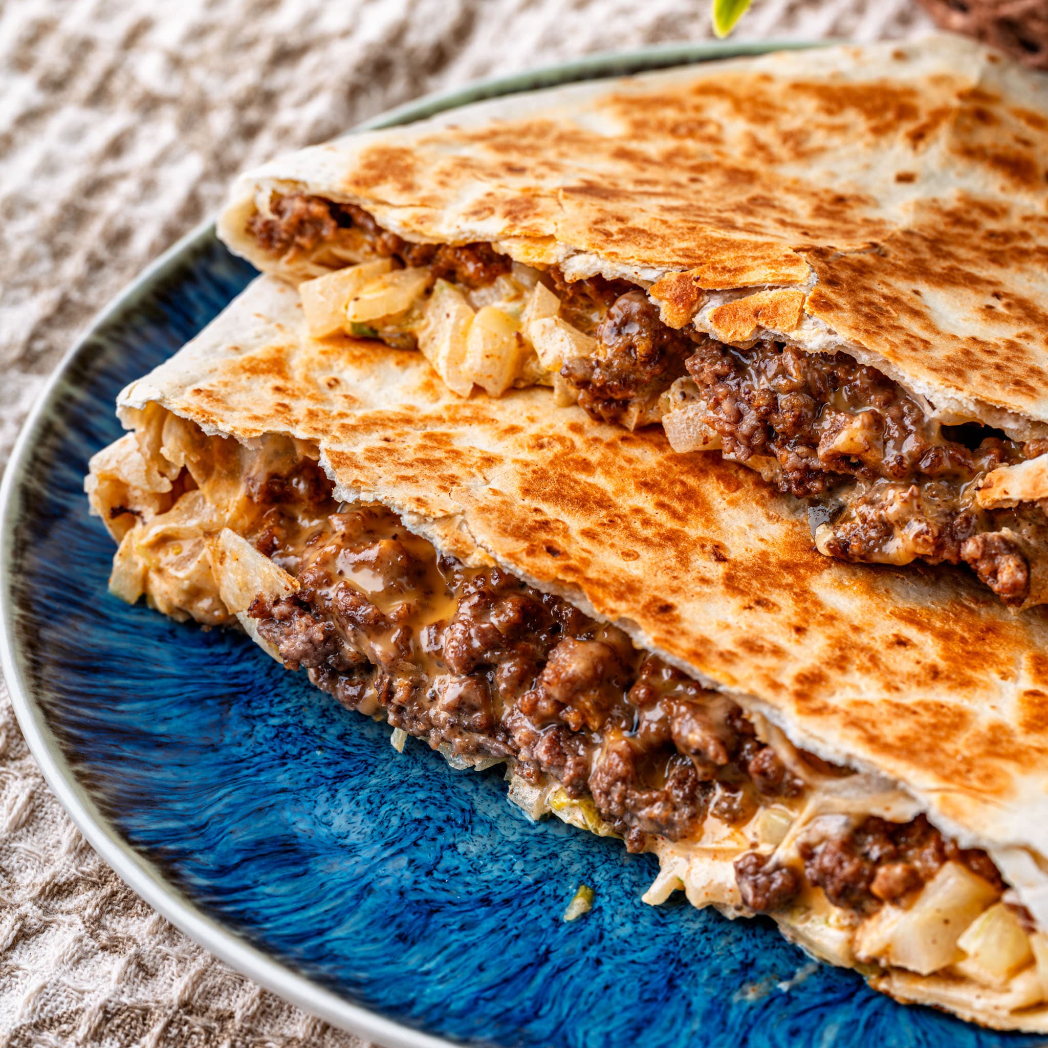A golden, seared crunchwrap sliced open to show the beef, cheese, and crisp lettuce inside.