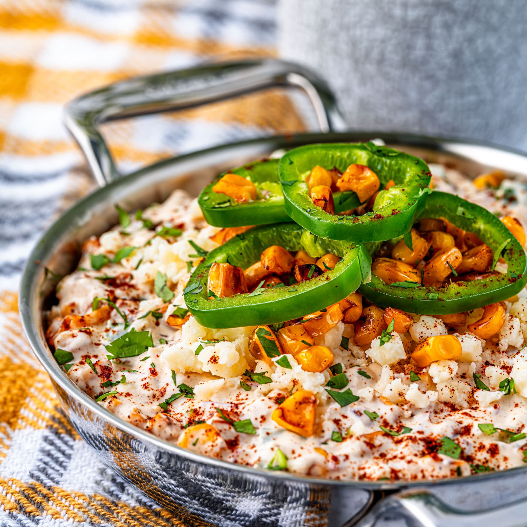 A bowl of warm street corn dip, cotija and cilantro scattered on top.