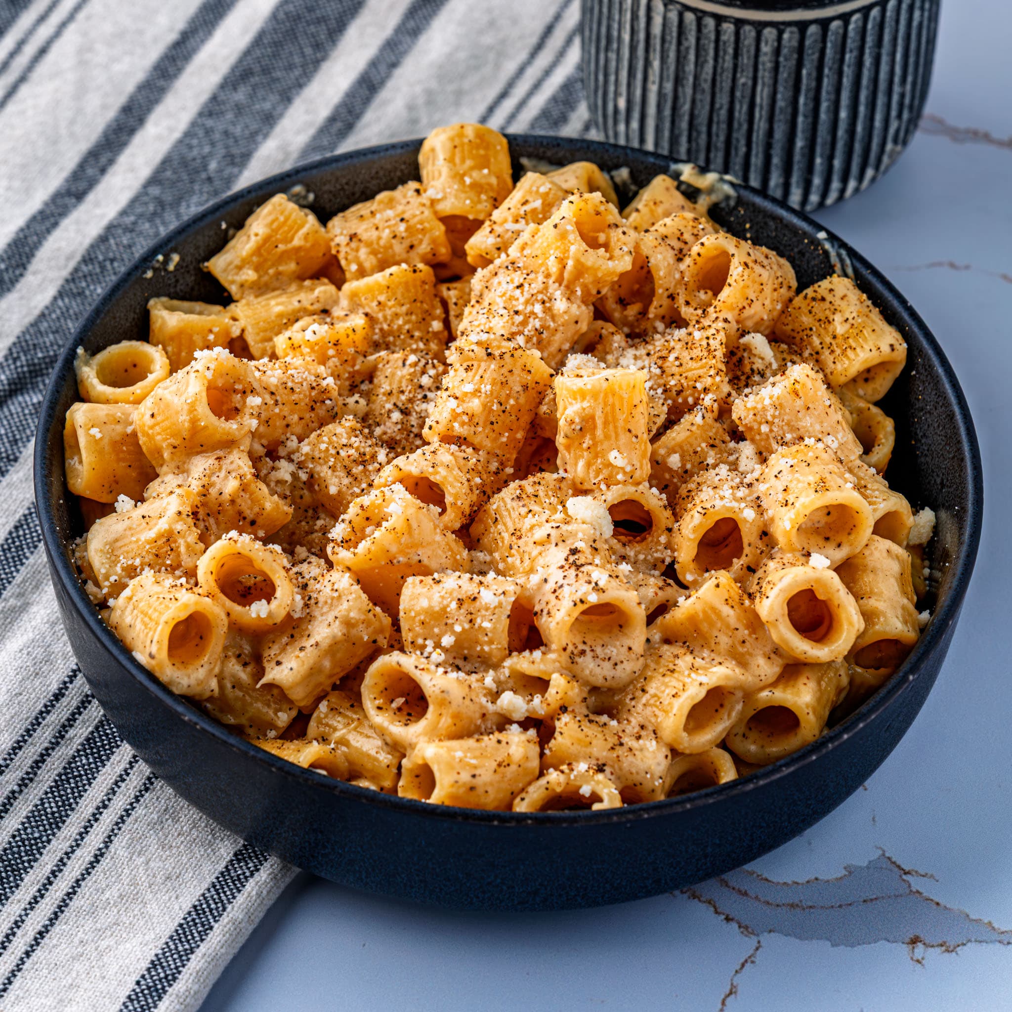 A steaming bowl of glossy mac and cheese, dusted with cracked black pepper and shaved pecorino.
