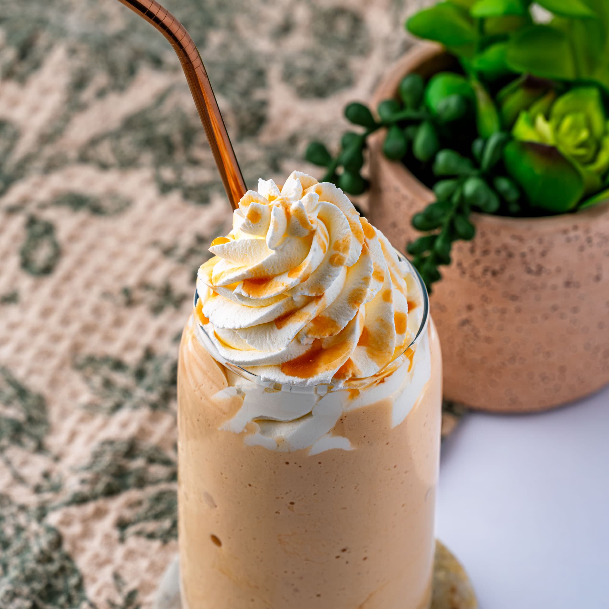 A tall glass of caramel frappuccino, swirled with whipped cream and caramel sauce.