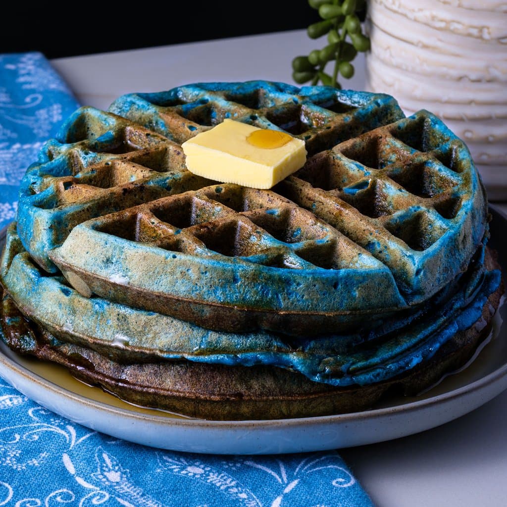 Golden-edged blue waffles stacked and topped with butter and maple syrup — breakfast just got a whole lot more fun.