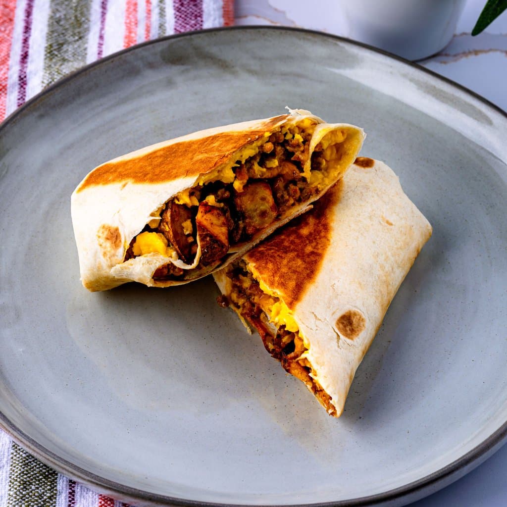 Golden-toasted breakfast burritos sliced in half, revealing layers of chorizo, egg, potato, and cheddar.