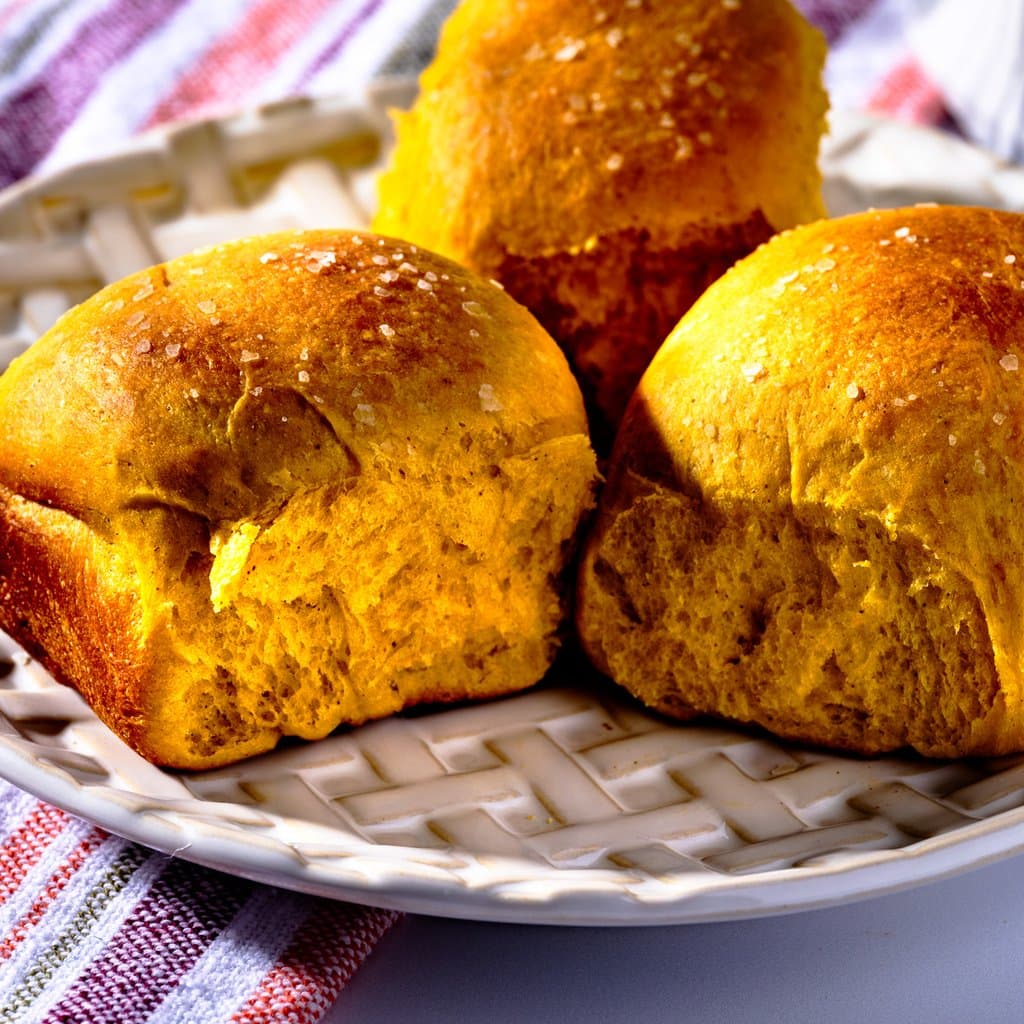 Freshly baked pumpkin dinner rolls, golden-amber on top, piled warm in a 9x13 dish.