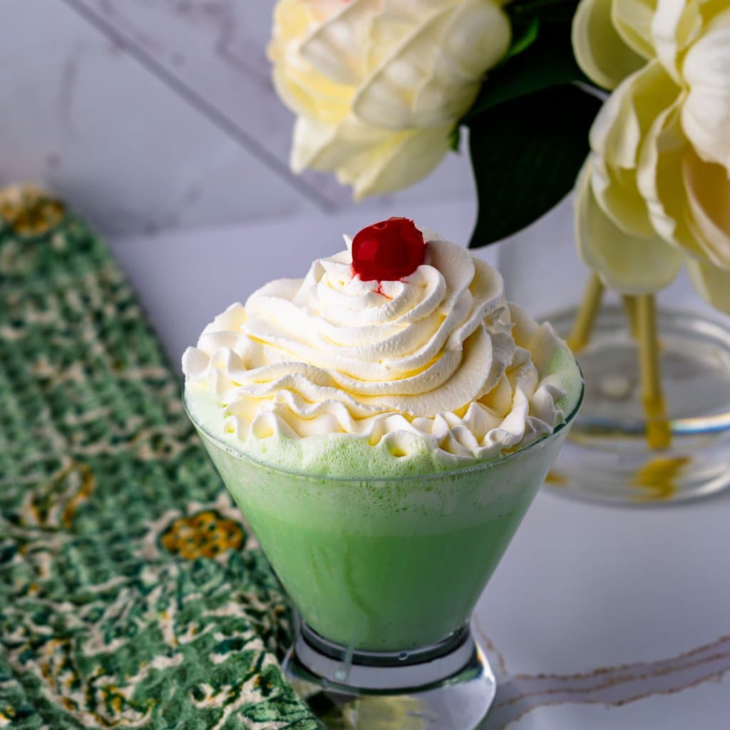 Homemade Shamrock Shake topped with whipped cream and a cherry — that iconic minty green in a tall glass.