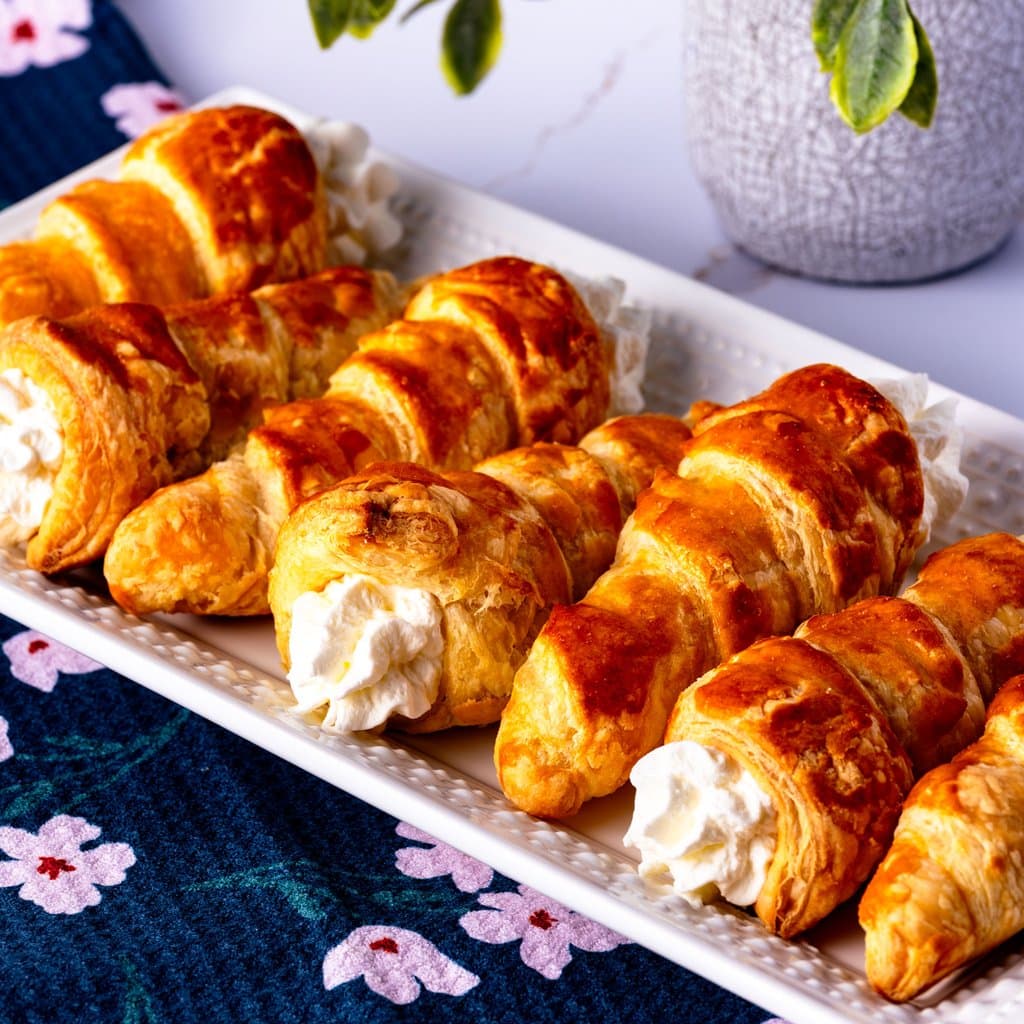 Golden puff pastry cream horns dusted with powdered sugar, filled with billowy whipped cream.