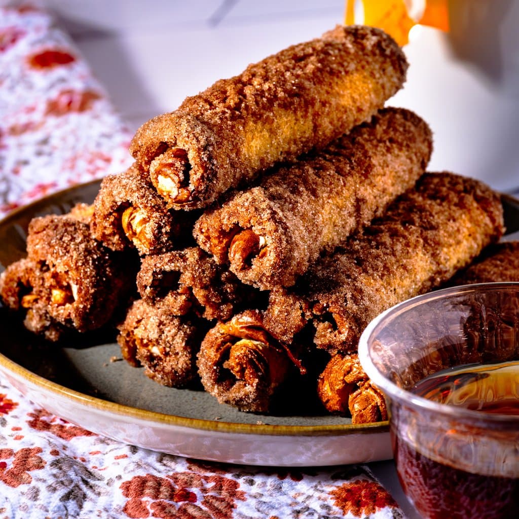 Golden, cinnamon-sugar-crusted roll ups fresh from the oven, served with a bowl of maple syrup for dipping.
