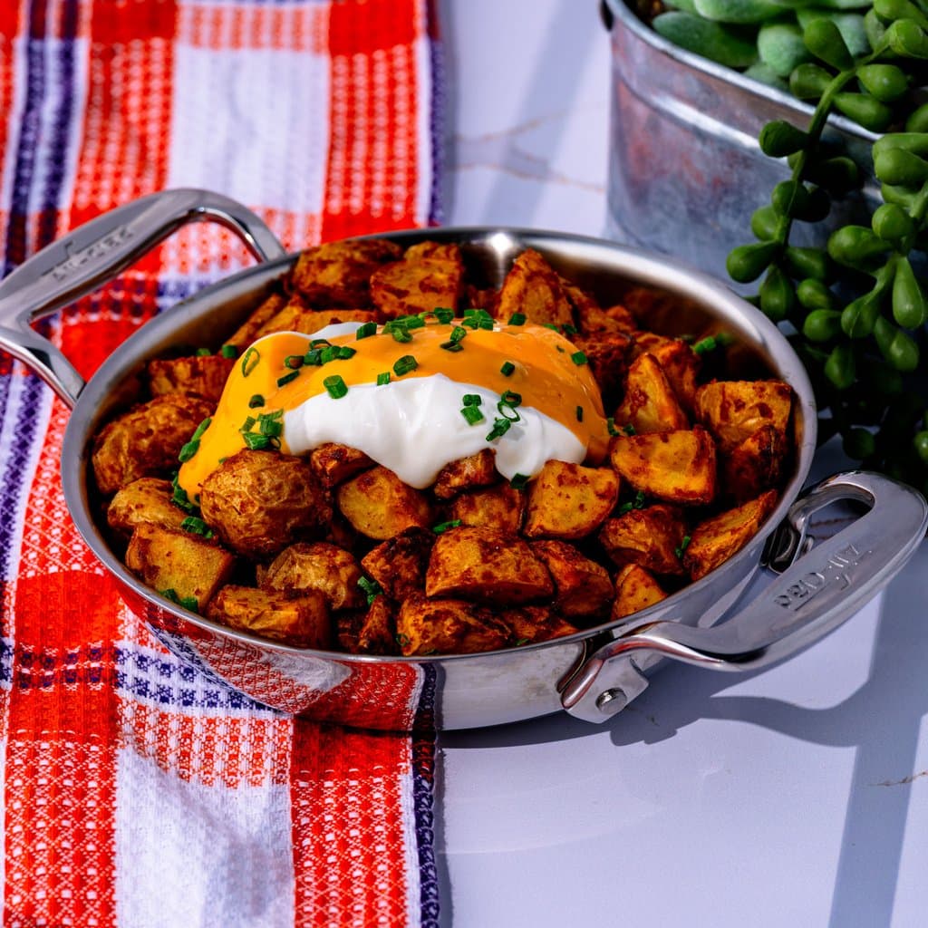 Cheesy Fiesta Potatoes fresh out of the air fryer, loaded with nacho cheese sauce, sour cream, and chives.