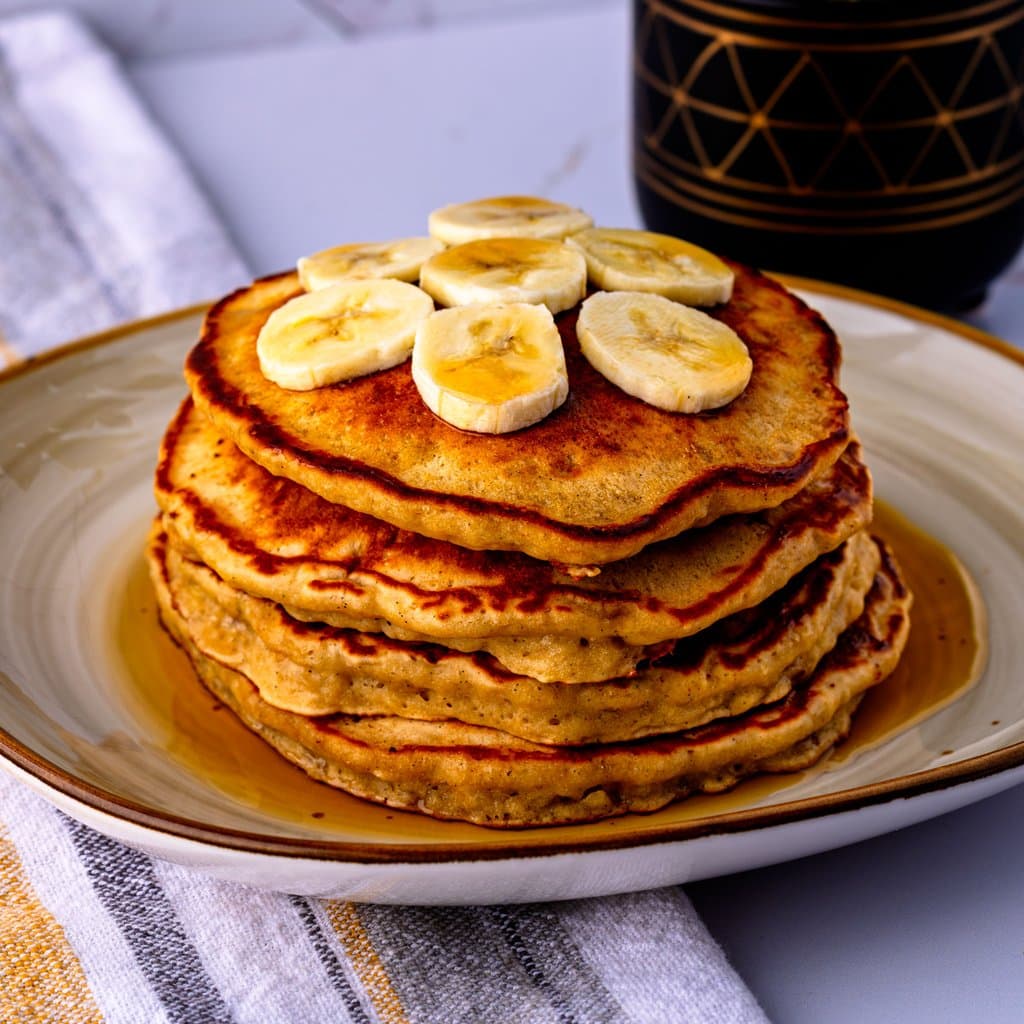 Golden brown sugar banana pancakes stacked high, topped with fresh banana slices and warm syrup.