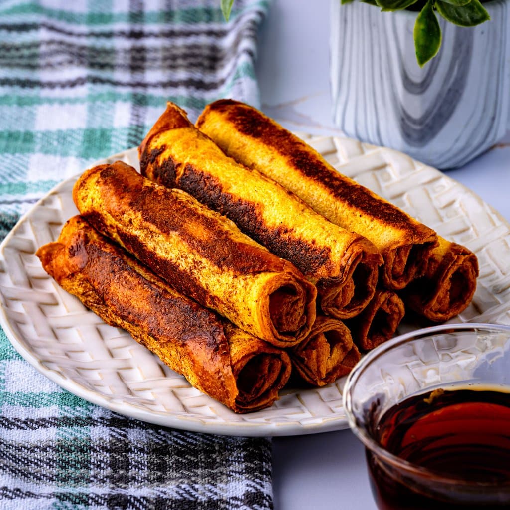 Golden French toast sausage roll ups served warm with a drizzle of syrup and a dusting of powdered sugar.